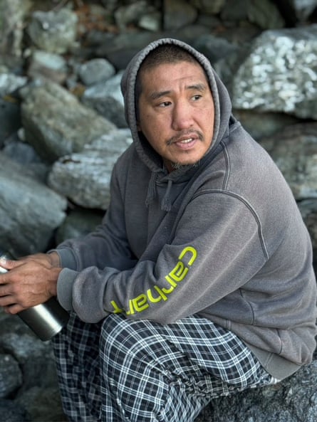 Man in sweatshirt and plaid pants sits on rocks.