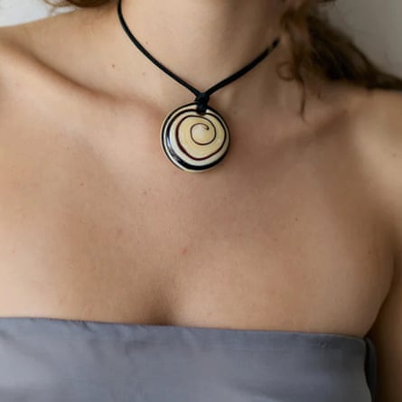 A close up of a leather necklace with cream and black swirl pendant against the collarbone of the model