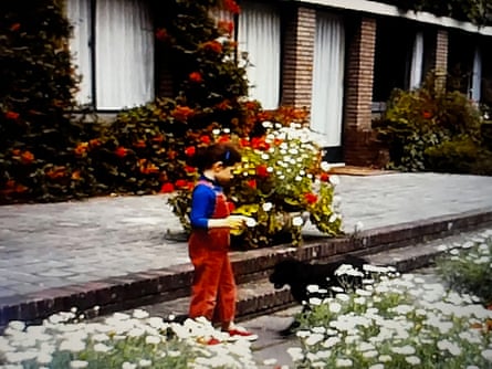 A vividly coloured photo of a dark-haired girl standing next to a black dog and surrounded by flower beds