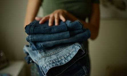 young woman, wearing green T-shirt, holding a pile of folded jeans in her both hands