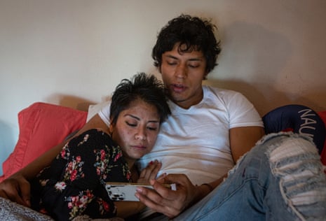 A man and woman lay in bed looking at a phone