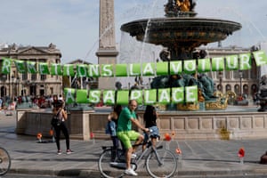 A man rides a bicycle in front of a fountain bearing the sign “let’s put the car back in its place” as he enjoys a vehicle-free day in Paris