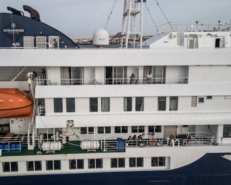 This aerial view shows passengers watching as unseen health personnel assists patients on to a boat from the cruise ship MV Hondius.
