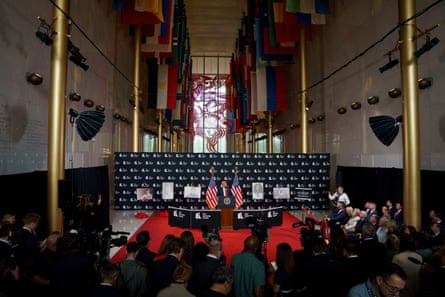 president unveils photographs in a gilded hall with hanging flags overhead while a crowd watches