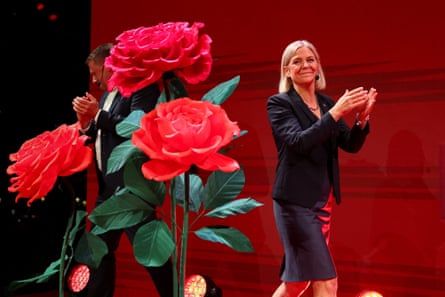 Magdalena Andersson claps while standing next to a large red roses emblem.
