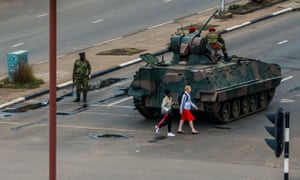 Young women walk past an armoured personnel carrier in Harare