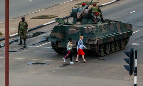 Young women walk past an armoured personnel carrier at an intersection in Harare.