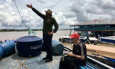 Dom Phillips sits on the seat of a boat as Bruno Pereira gestures across the water.