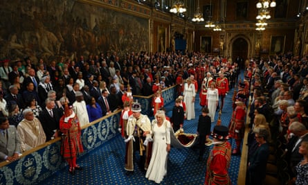 King Charles and Queen Camilla walk through the Royal Gallery with lots of people looking on
