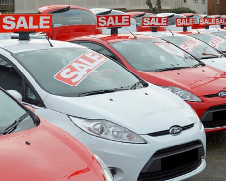 a used-car showroom with cars plastered in red and white sale stickers