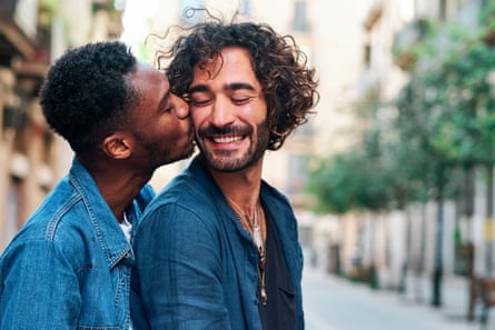 A man kissing his happy boyfriend on the cheek.