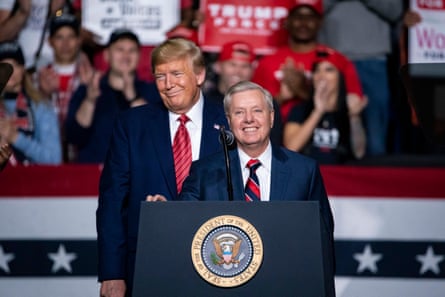 man in suit stands at podium smiling as another man in suit looks into crowd with a smile