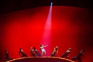Dua Lipa performs a concert flanked by dancers, against a red background