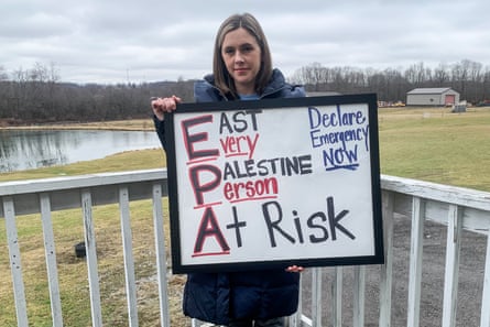 A woman holds a sign that reads “every person at risk, declare emergency now”