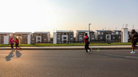 Three women and one man in running gear run down a road in front of newly built houses.