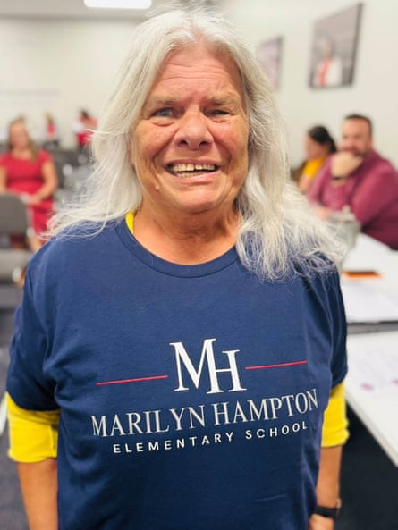 A woman smiles, wearing a navy T-shirt with her name, indoors