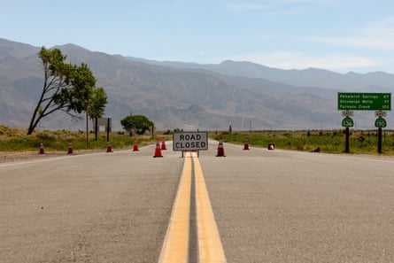 A flat two-lane highway facing hills with orange cones blocking it.