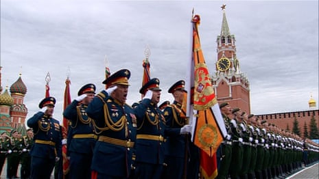 Some uniformed Russian service members stand in salute alongside other Russian service members in tidy lines in Moscow's Red Square under a cloudy gray sky.