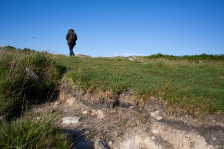 A man walks on grass next to an area where the land has opened up to expose soil and rocks.