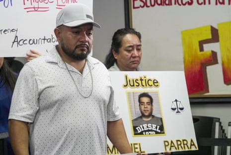 Miguel Parra Hernandez's family stand solemnly beside a sign reading "Justice" with his mugshot
