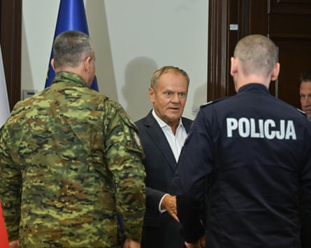 The Polish prime minister, Donald Tusk, centre talks to a police chief and military chief, whose backs are to the camera
