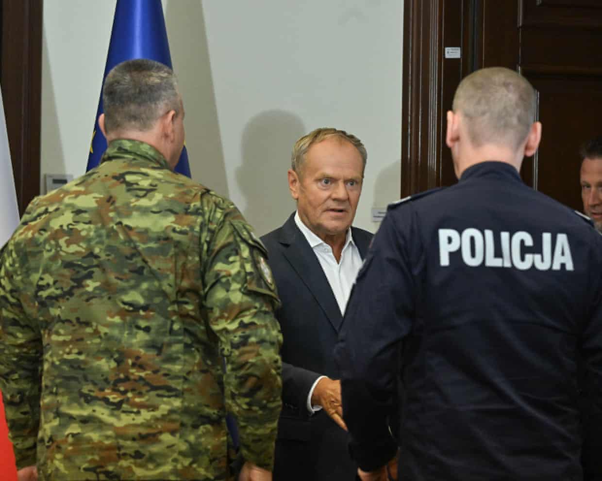 The Polish prime minister, Donald Tusk, centre talks to a police chief and military chief, whose backs are to the camera