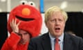 Boris Johnson speaking as a Monster Raving Loony
party candidate lifts his costume to wipe his forehead in the background