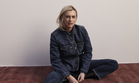 Gracie Otto is sitting cross-legged on the floor against a white wall, she is wearing denim jeans and a denim jacket