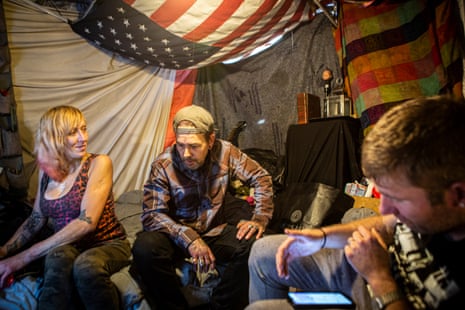 Two men and women sit inside a tent with an American flag on the ceiling