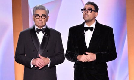 two men wearing black glasses, suits and bowties stand next to each other