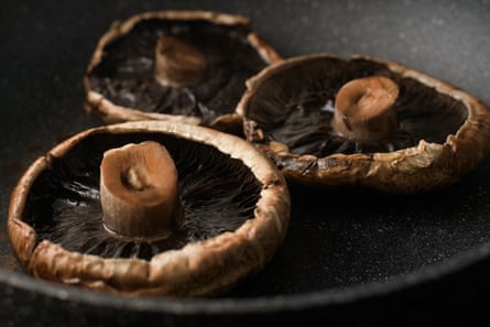 Three portobello mushrooms being seared in a pan.