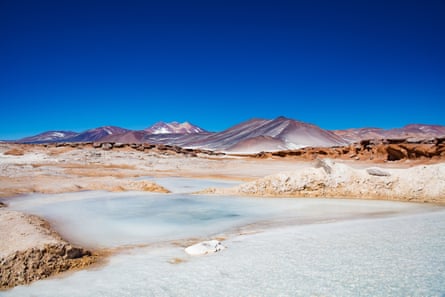 Salt flats mingle with the red rocks of the Atacama desert, under a deep blue sky.