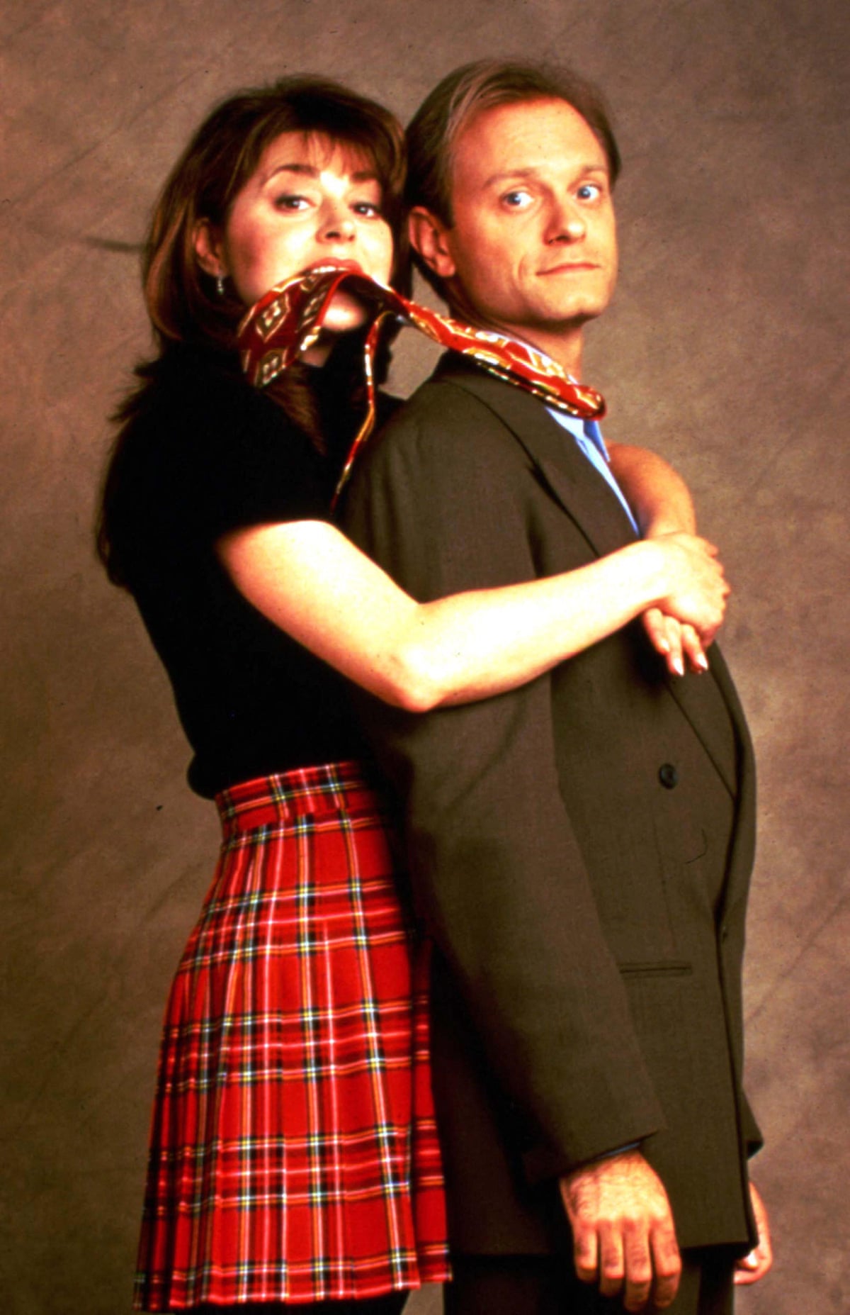 The stand side-on to the camera, her behind him, with his tie in her mouth