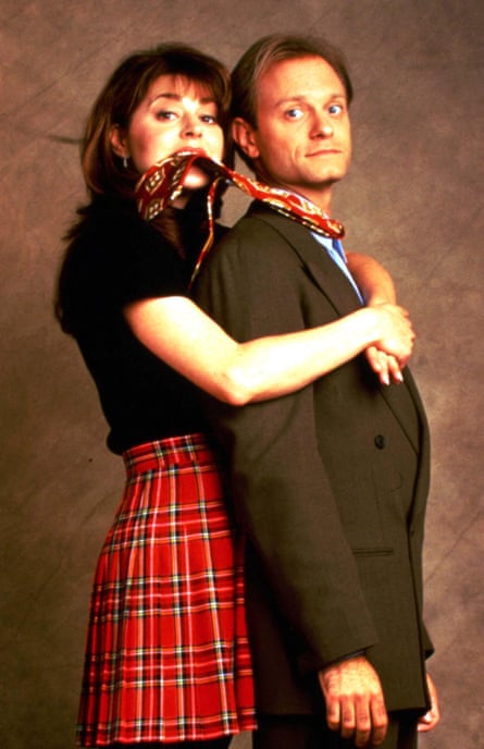 The stand side-on to the camera, her behind him, with his tie in her mouth