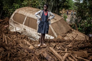 A girl stands next to a damaged car buried in mud at an area heavily affected by torrential rains and flash floods in the village of Kamuchiri, Kenya.