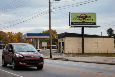 A street scene with a billboard showing the words ‘Industrial Solar Plants’ crossed out in red.