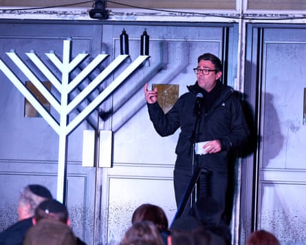 Andy Burnham speaking next to a large menorah