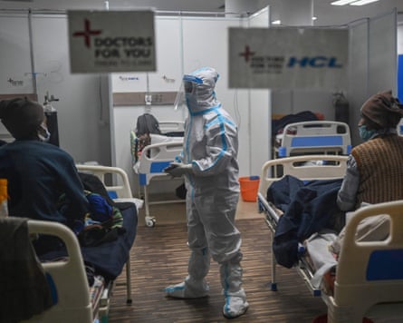 A person wearing protective medical gear talking to people sitting in hospital beds