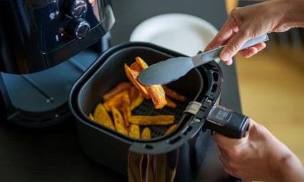 A woman is using an air fryer to prepare food in her kitchen, focusing on a healthier cooking method with minimal oil.