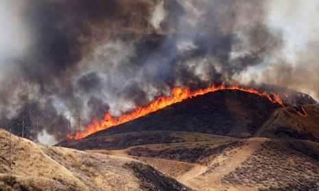 wildfire burning across the top of a hill with black smoke swirling in the sky overhead