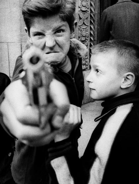 Image of a young boy pointing at the camera with a guy while watched by a younger boy