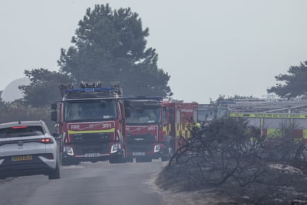 Several fire engines on a road, with a thin pall of smoke in the air