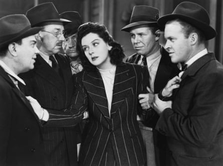 Hildy in sharp pinstripe suit, is surrounded by men who are all looking at her