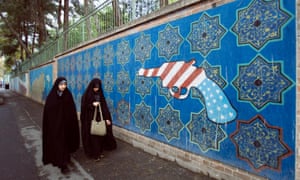 Iranian women walk past a mural outside the former US embassy in Tehran.