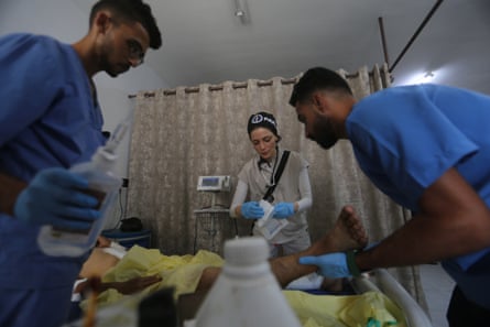 Three doctors attend to a patient who is obscured from view in a Gaza hospital ward.