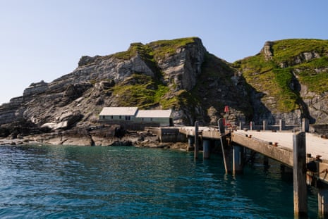 View of a wooden jetty and some low wooden buildings on the rocky outcrop of Lundy, blue sky, calm sea.
