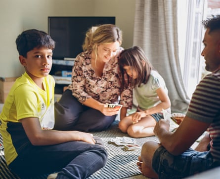 The family sit playing a card game on the floor of their living room
