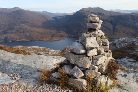A cairn on a high mountain path overlooking a loch with surrounding mountains