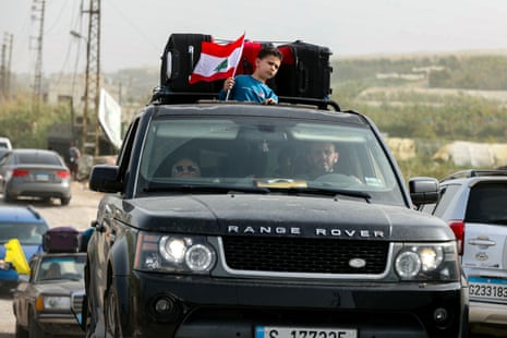 A boy stands out of the sunroof of a car holding a Lebanese flag.
