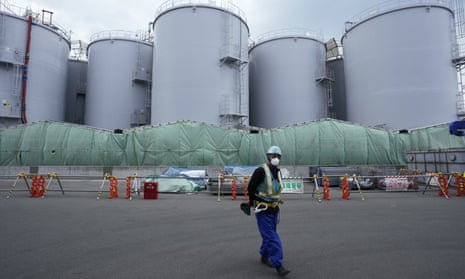 A worker helps direct a truck driver as he stands near tanks used to store treated radioactive water after it was used to cool down melted fuel at the Fukushima Daiichi nuclear power plant